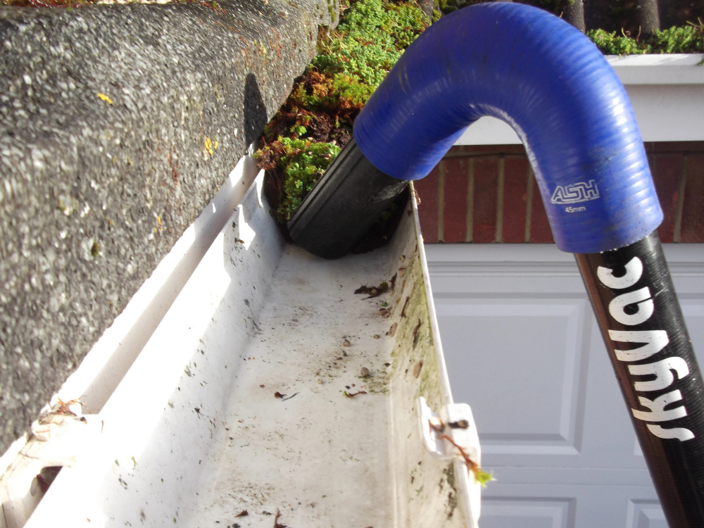 A gutter vacuum nozzle lifting moss out of a white plastic gutter