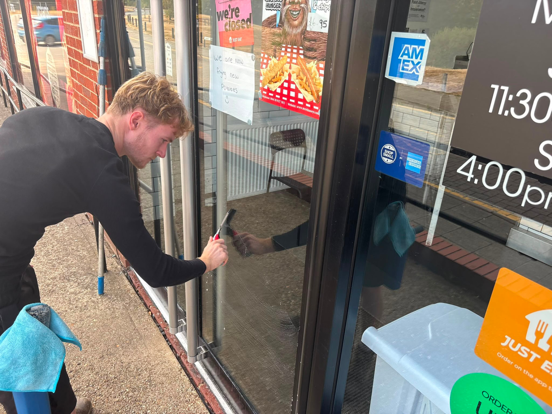 Shopfront glass being squeegeed by hand at a local takeaway